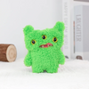A bright green, fuzzy monster plush toy with yellow eyes sits on a white surface.