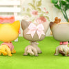 A set of three LPS-style vinyl cat figurines in yellow, beige, and brown with matching scarf necklace accessories on a green 