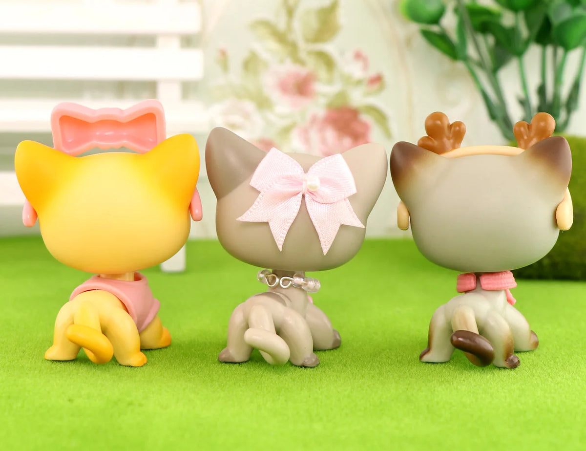 A set of three LPS-style vinyl cat figurines in yellow, beige, and brown with matching scarf necklace accessories on a green 