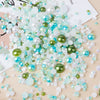 A scatter of mixed resin rhinestone pearls in shades of white, blue, and green on a light wooden surface.