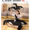 A woman is holding a black and white orca whale plush toy in a clean home setting.