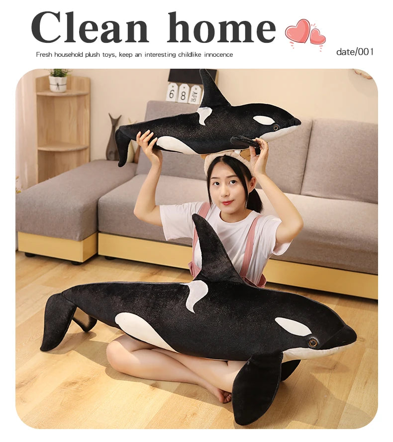 A woman is holding a black and white orca whale plush toy in a clean home setting.