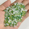 A hand holds a pile of natural tumbled stone chips in shades of green and clear white for jewelry making