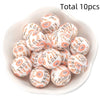 A bowl filled with ten small, round, white silicone beads decorated with orange and black floral patterns.