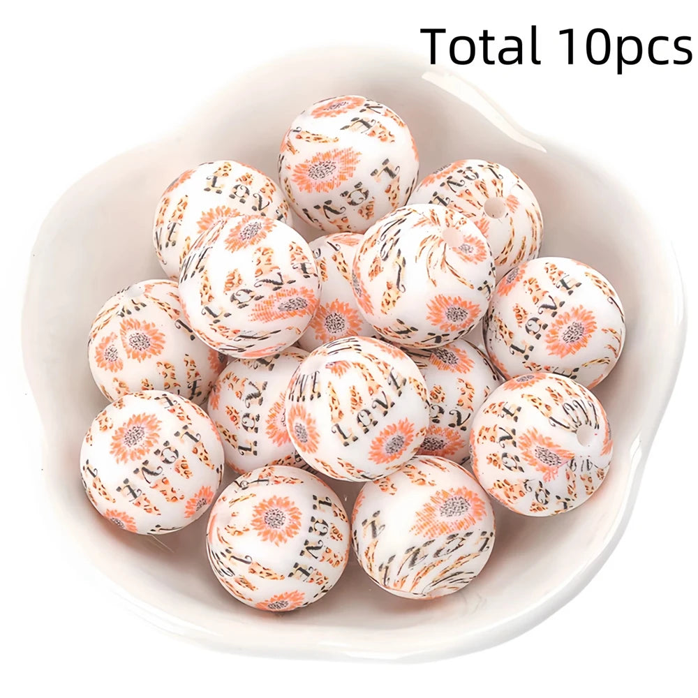 A bowl filled with ten small, round, white silicone beads decorated with orange and black floral patterns.