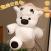 A white plush toy resembling a calf or cow with black markings, being held by a hand.