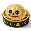 A golden pumpkin-shaped squishy fidget toy with a carved face sits in a yellow and black slotted container.
