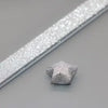Silver glitter origami star paper strips laid diagonally on a gray surface.