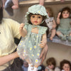 A realistic silicone vinyl toddler doll named Betty is being held by a person, with other dolls visible in the background.