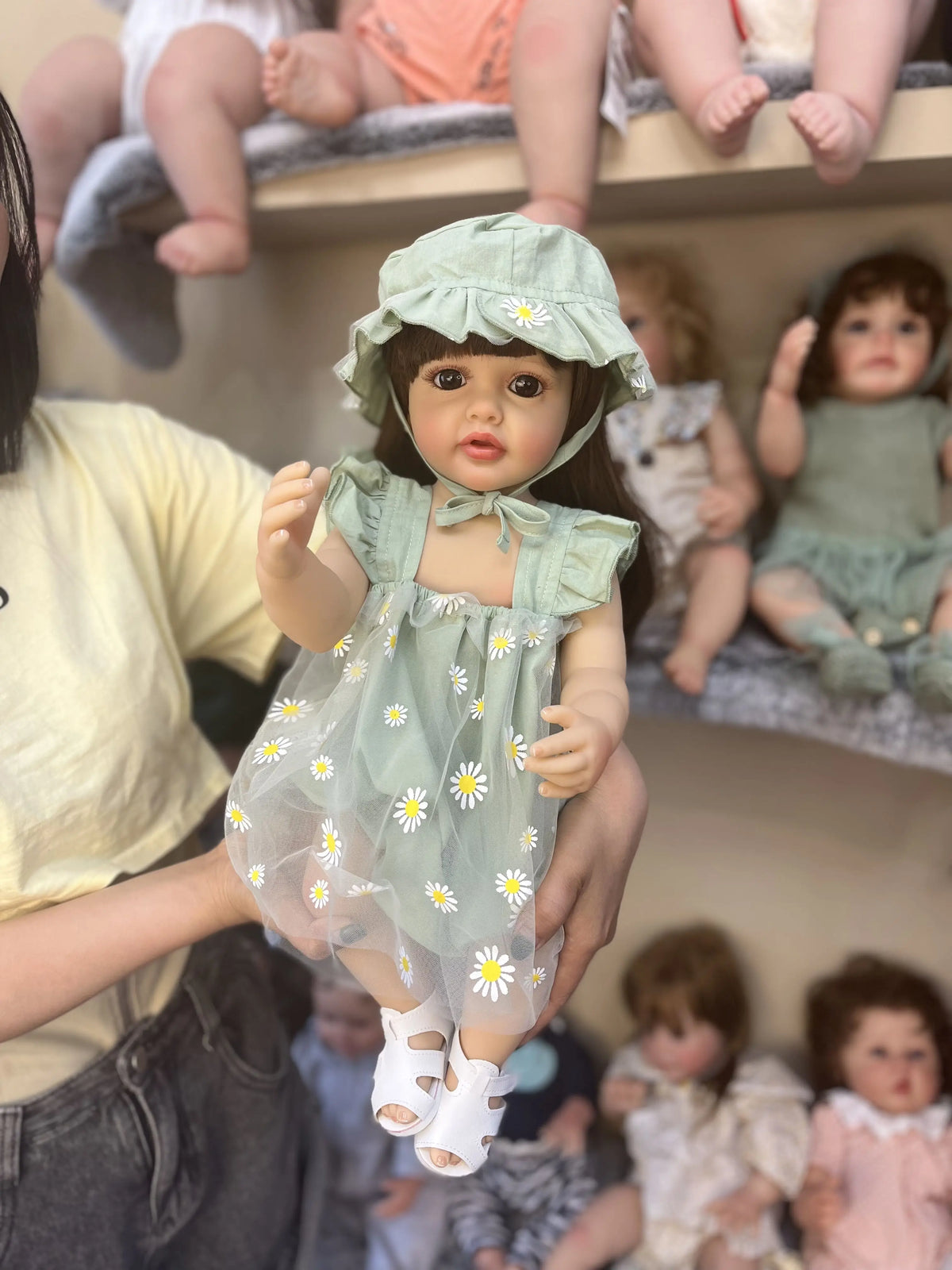A realistic silicone vinyl toddler doll named Betty is being held by a person, with other dolls visible in the background.