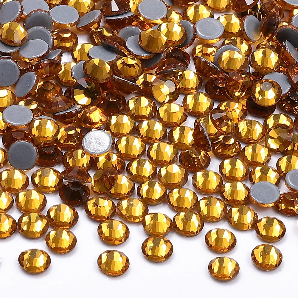 A close-up view of small, faceted glass crystal hot fix rhinestones in various shades of amber and gold.