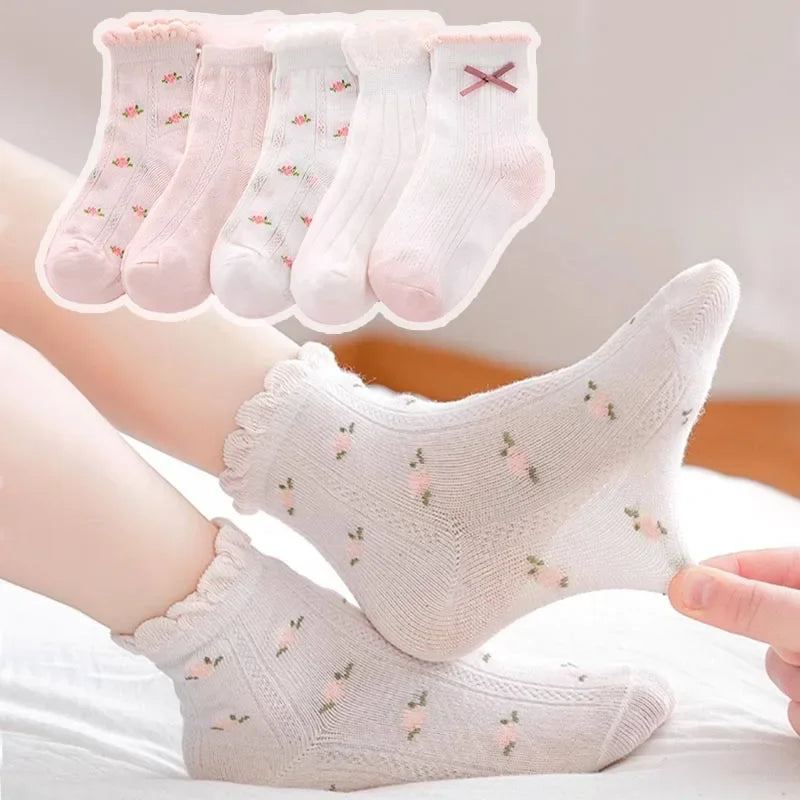 A stack of five pink floral cotton kids socks and one larger white sock are shown on a person's foot.
