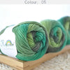A stack of bright green merino wool yarn skeins in various shades are displayed on a wooden board.