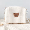 A white quilted baby diaper caddy organizer with a brown bear patch on the front, resting on a cream knit fabric.