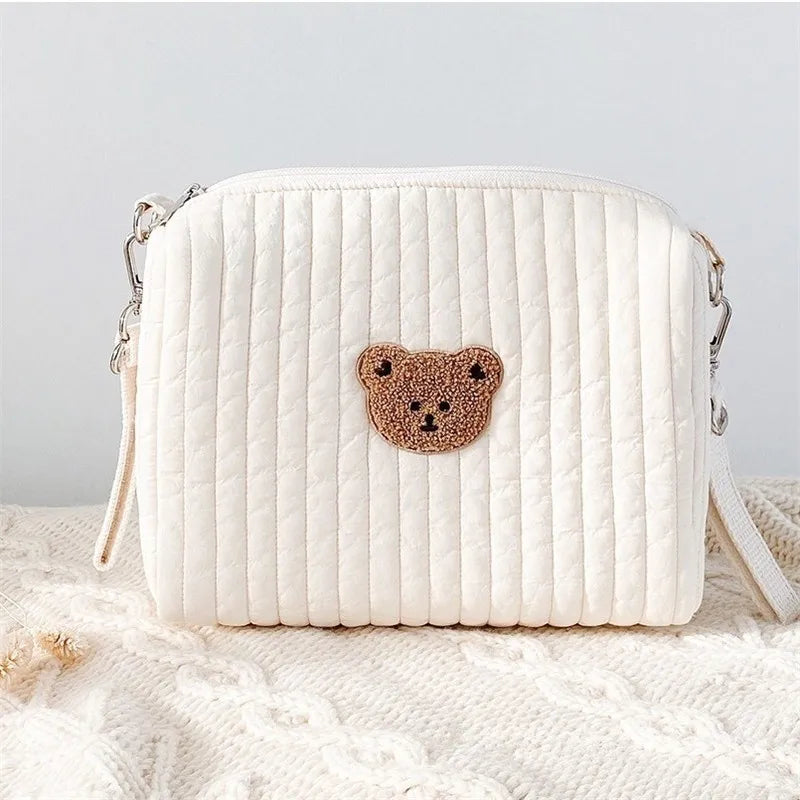 A white quilted baby diaper caddy organizer with a brown bear patch on the front, resting on a cream knit fabric.