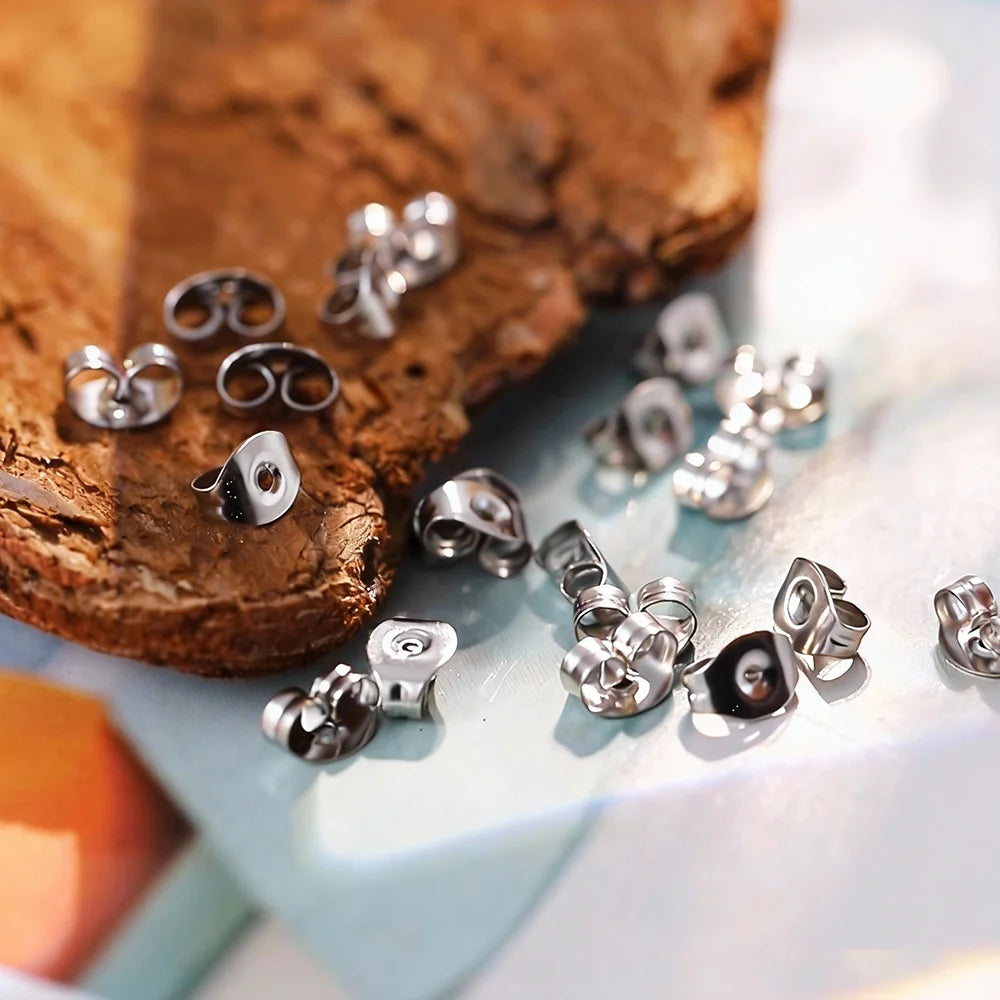 A collection of stainless steel earring stud bases and backs laid out on a wooden surface.
