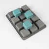 A silicone soap mold with 12 square cavities, featuring a mix of gray and teal silicone pieces.