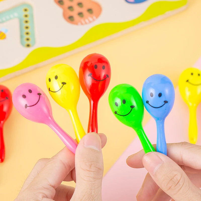 A hand holds several colorful mini maracas shaker toys in various bright colors like yellow, pink, red, and green.
