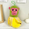 A green and pink plush toy resembling a monkey wearing a yellow garment sits on a white surface.
