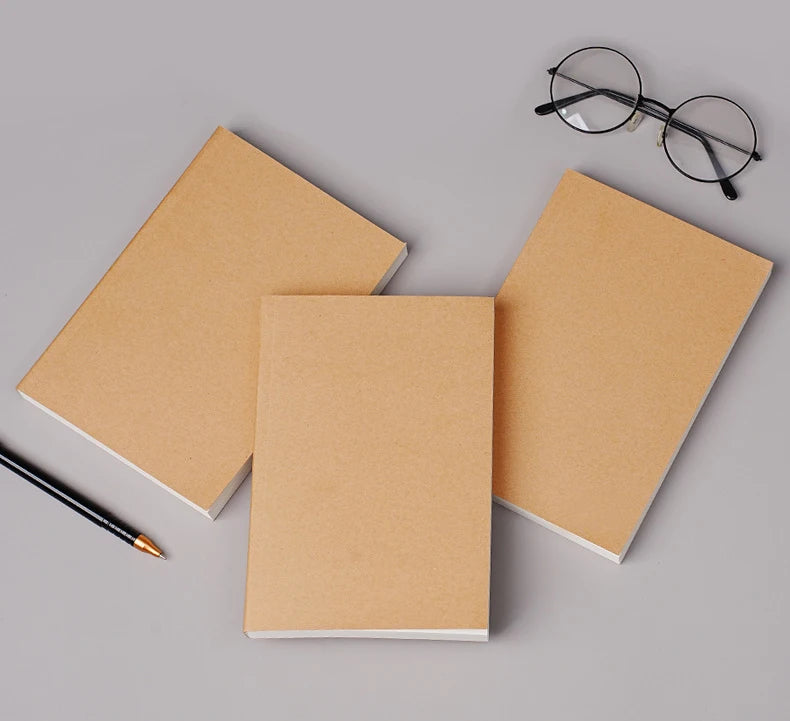A stack of blank kraft paper notebooks and a black pen are displayed on a gray surface.