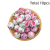 A collection of ten pink and white floral printed silicone beads arranged on a wooden plate.