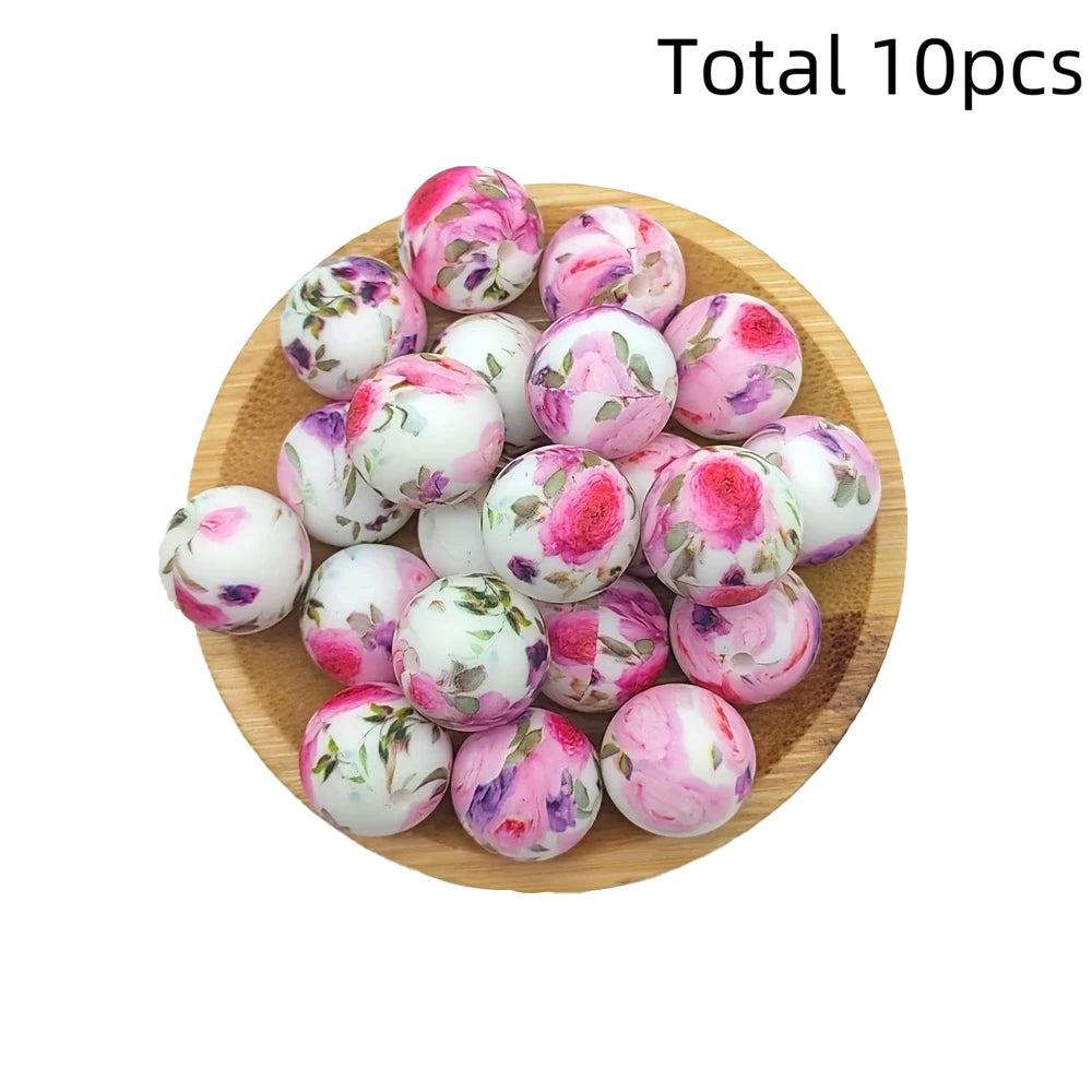 A collection of ten pink and white floral printed silicone beads arranged on a wooden plate.