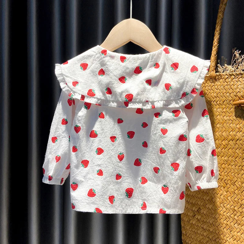 White long-sleeve shirt for a baby girl with a red strawberry print, displayed on a wooden hanger.