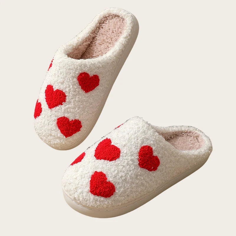 A pair of white plush indoor slippers with red heart accents.