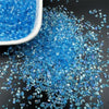 Blue crushed glass crystals in a white bowl and scattered on a dark surface for resin and jewelry making