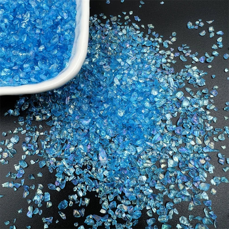 Blue crushed glass crystals in a white bowl and scattered on a dark surface for resin and jewelry making