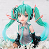 A PVC figure of Hatsune Miku with teal hair and headphones, displayed on a white floral arrangement.