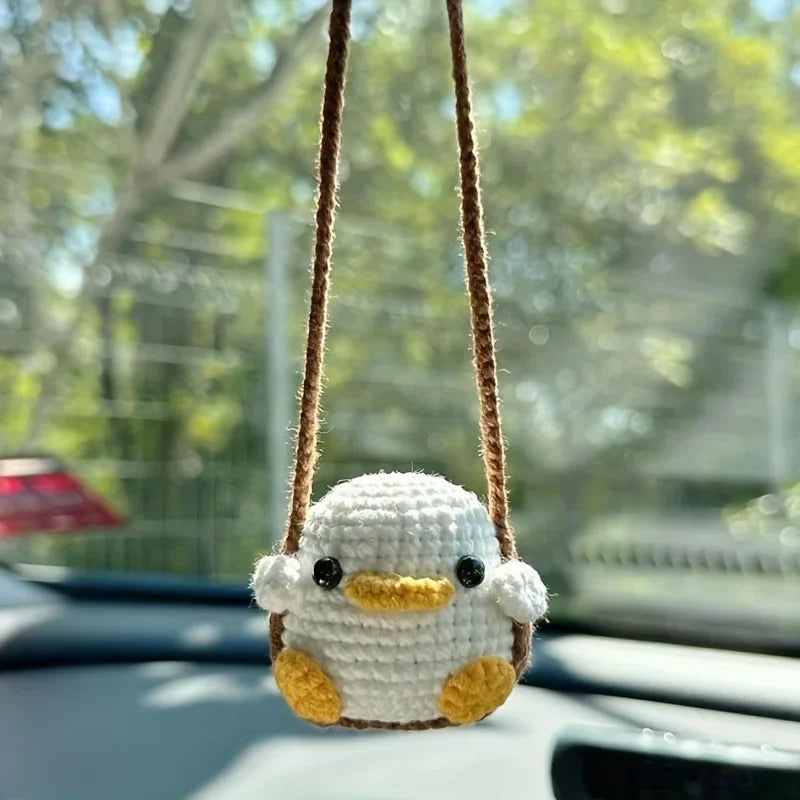 Handmade crochet animal car hanging ornament with a yellow beak and white body suspended by a brown string.