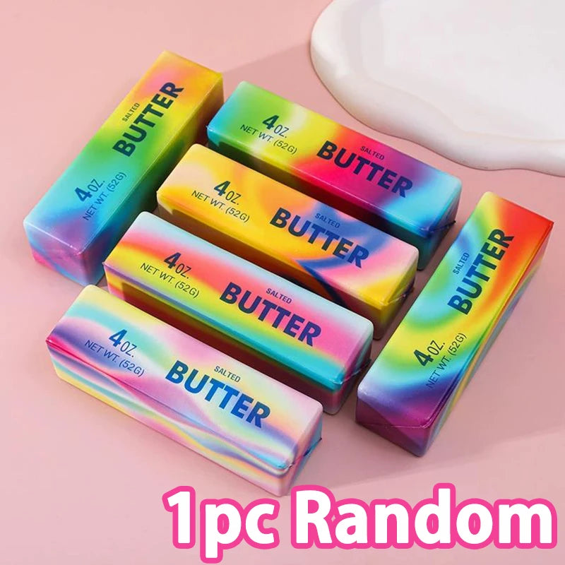 A random assortment of five squishy butter toys in various colors and sizes are displayed on a pink background.