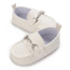 A pair of white baby first walker sneakers with a dinosaur print detail and silver hardware.