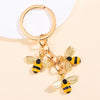 Gold-toned enamel flower keychain featuring a bee design on a circular split ring.