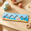 A wooden sensory activity board for toddlers featuring a wavy design and a small plastic toy.