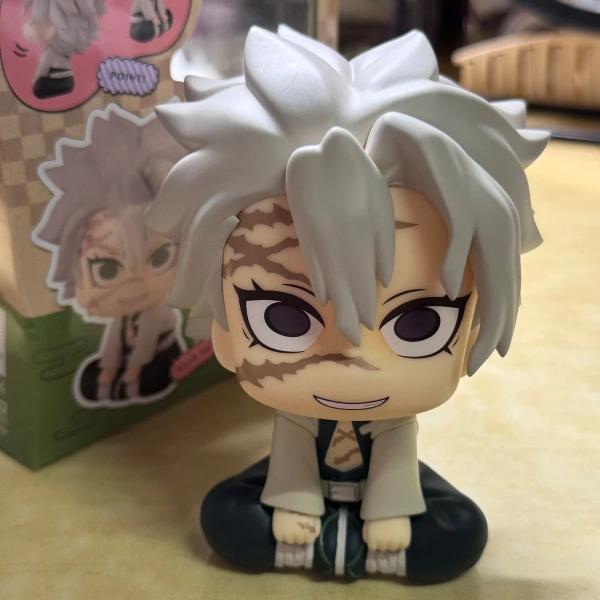A figure of Tanjiro Kamado from Demon Slayer, featuring white hair and a striped face, displayed next to packaging.