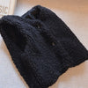 A black, chunky knit lamb wool vest with a V-neck and buttons is displayed on a light surface.