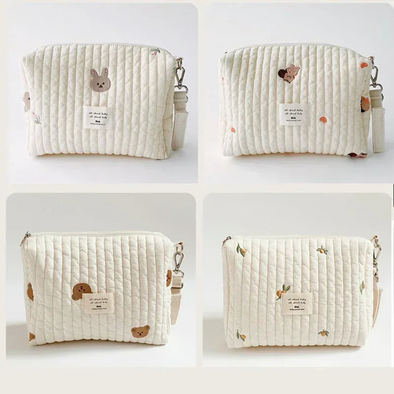 A cream quilted baby diaper caddy organizer with small animal embroidery and attached stroller straps.