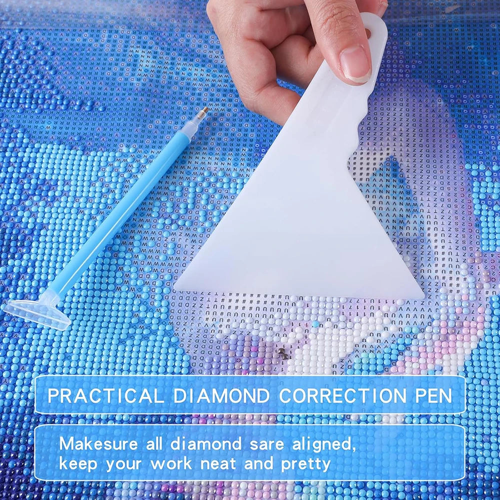 A hand holds a white diamond correction pen on a blue diamond painting surface.