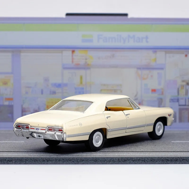 A diecast model of a 1967 Chevrolet Impala in cream color displayed on a gray surface.