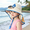 A young woman wearing a beige sun hat with a blue fabric and a USB charging fan attached, standing near the ocean.