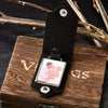 A black leather keychain featuring a custom photo and personalized engraving resting on a wooden box.