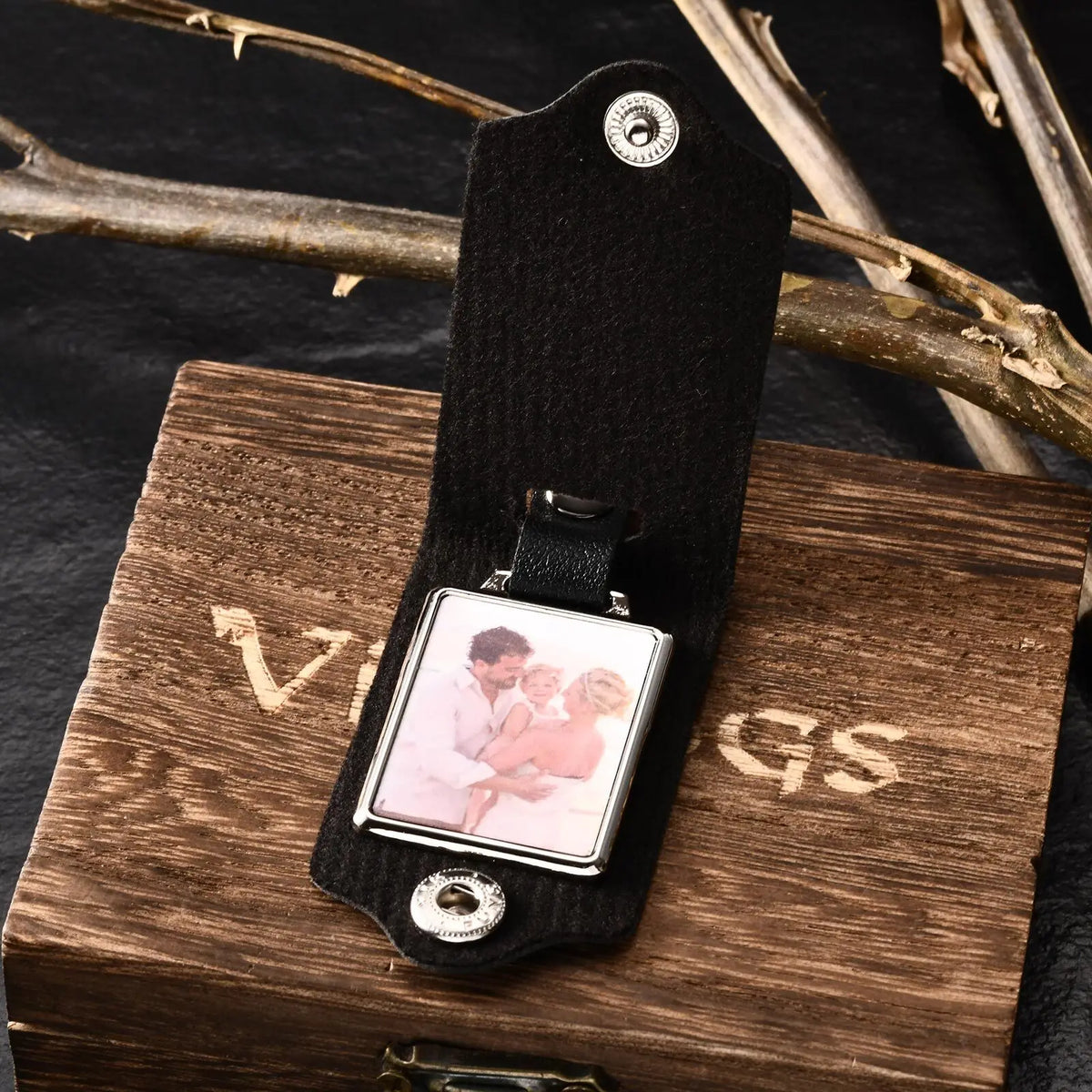 A black leather keychain featuring a custom photo and personalized engraving resting on a wooden box.