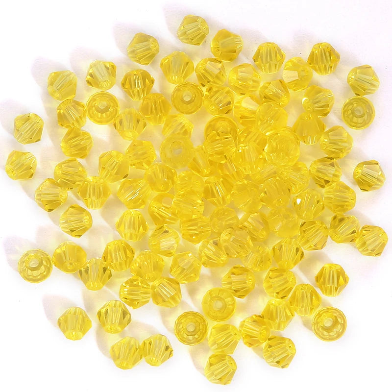 A pile of small, faceted, yellow glass beads shaped like bicones for jewelry making.