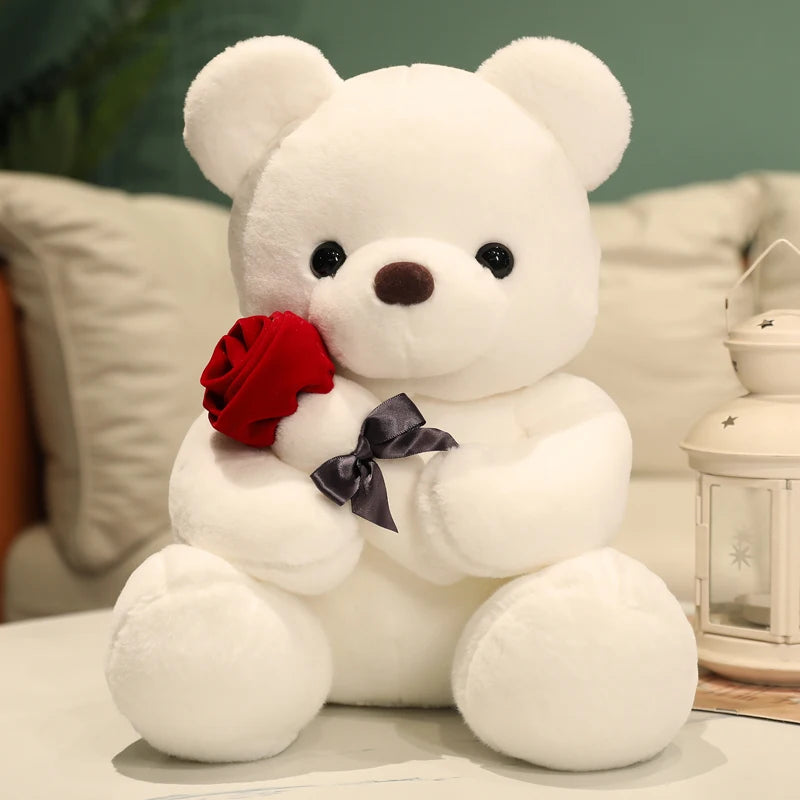 A white teddy bear plush toy holding a red rose, sitting on a light surface.