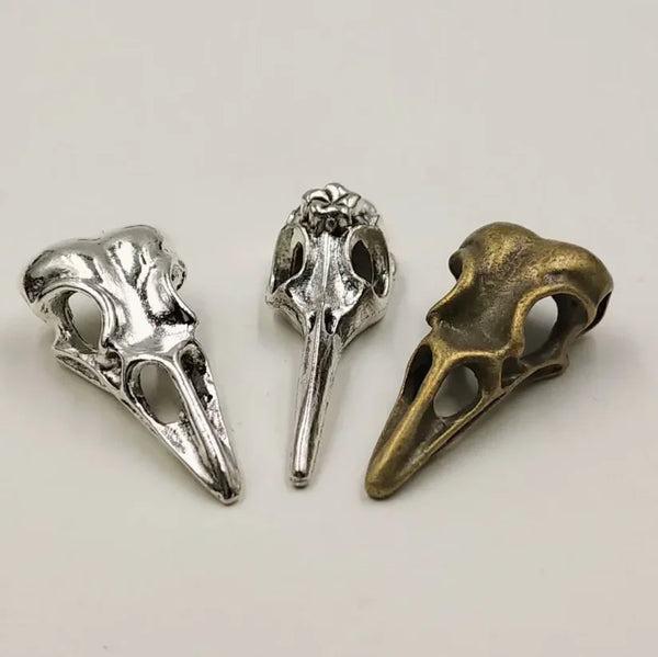 Two silver and bronze gothic skull bird head pendants displayed on a white background.