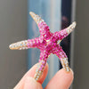 A pink and gold rhinestone turtle brooch pin is held by a person's fingers.