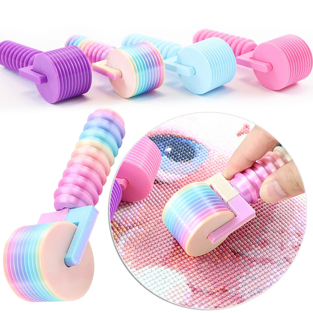 Assortment of colorful, detachable diamond painting rollers and a hand demonstrating their use on a pink surface.