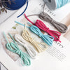 A collection of various colored braided ribbon rolls in blue, pink, white, and gray laid out on a white surface.